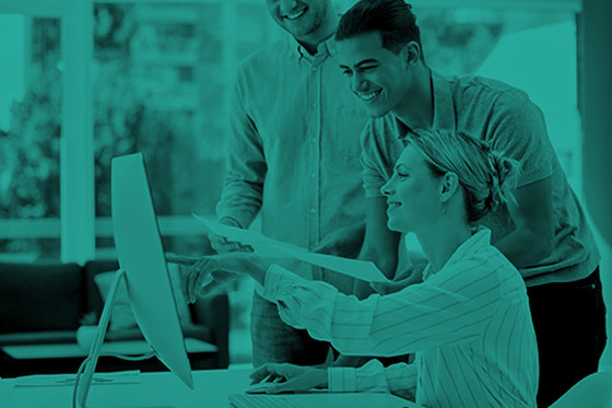 Three people by a desk looking at a computer